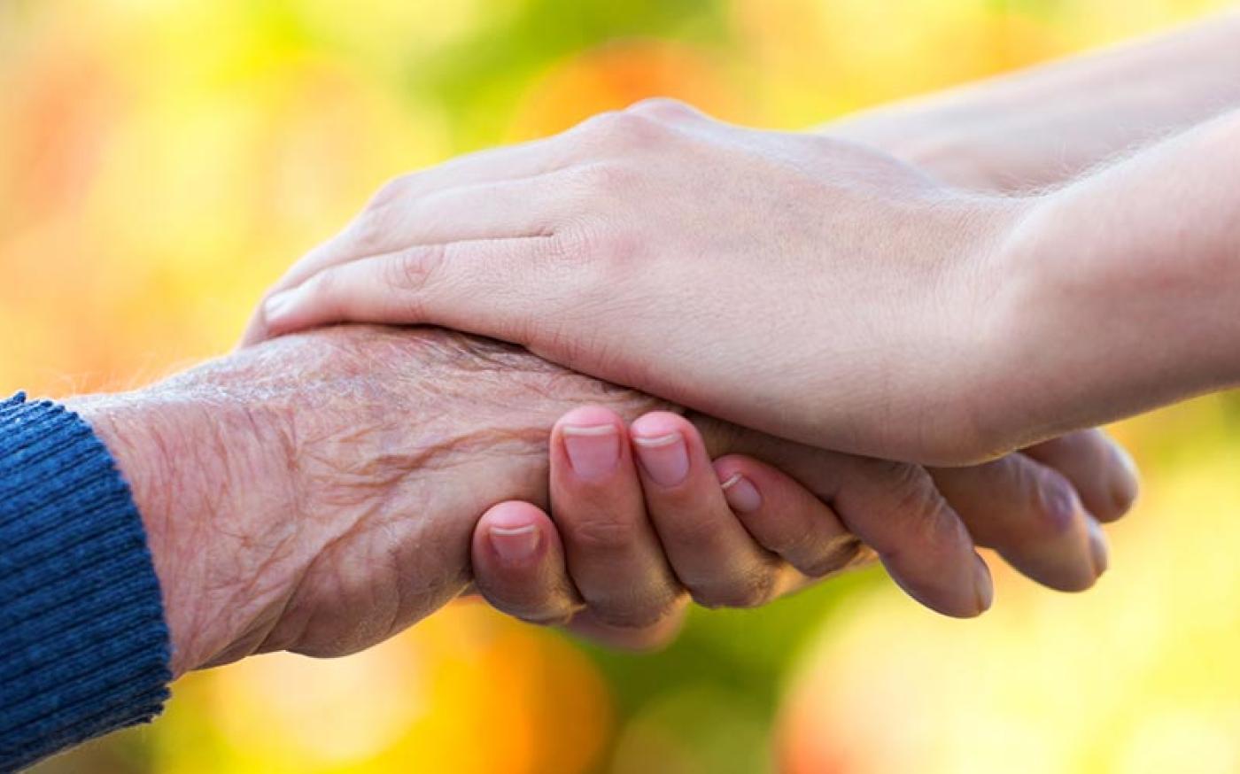 Close-up image of an elderly hand being held by a younger-looking hand